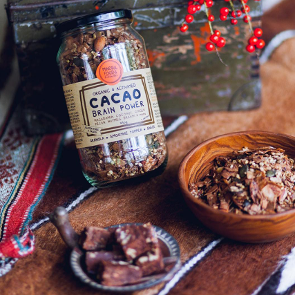 Glass jar of Cacao Brain Power Granola with some chocolate slices and a bowl of granola next to it.'
