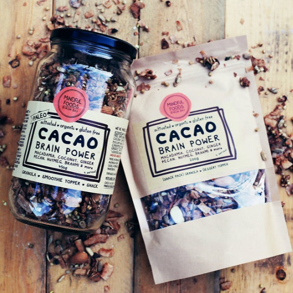 450g glass jar of cacao brain power granola lying next to 200g cacao brain power granola in compostable bio-bag.