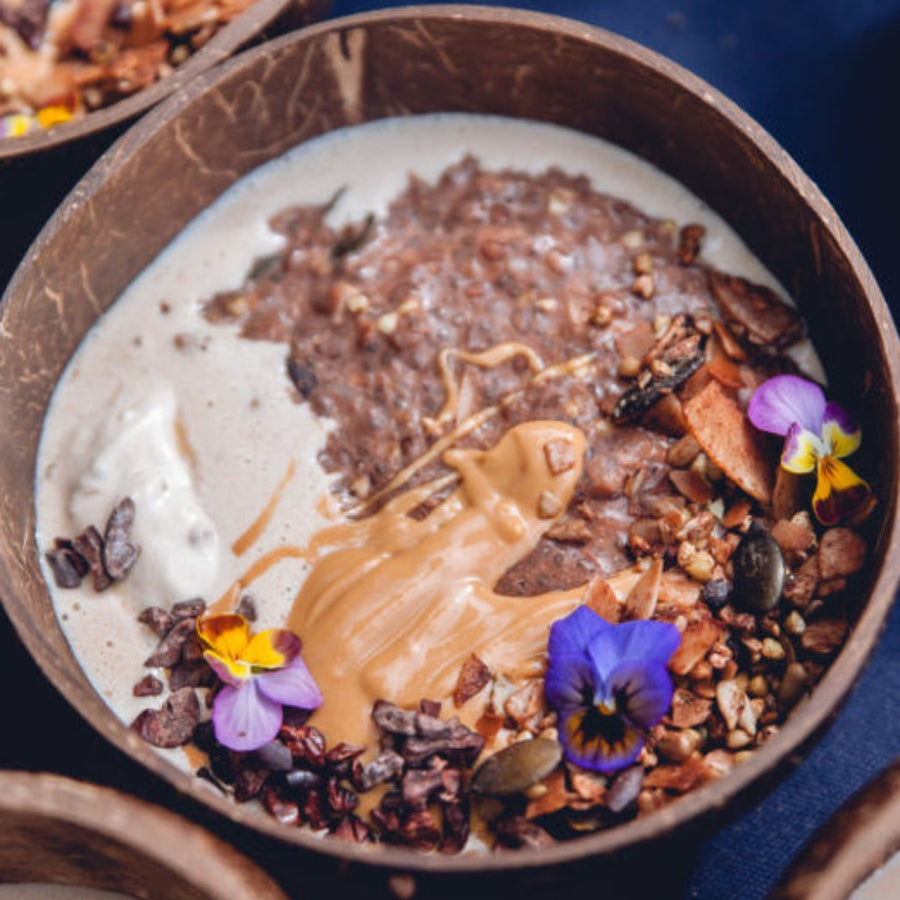 Bowl of porridge made from birchia and cacao brain power granolas with edible flowers to garnish