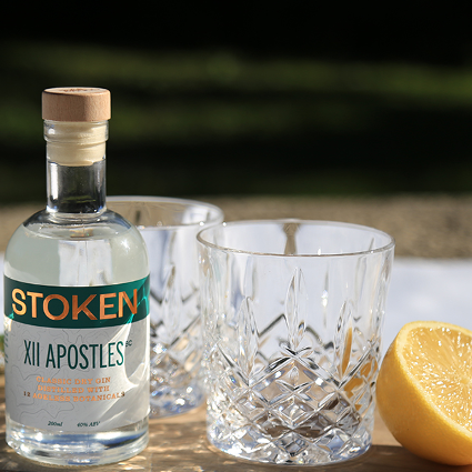 a 200ml bottle of Stoken XII Apostles classic dry gin next to 2 short glass tumblers and half a lemon