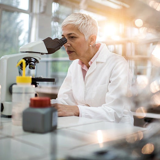 female scientist in white laboratory coat looking into microscope